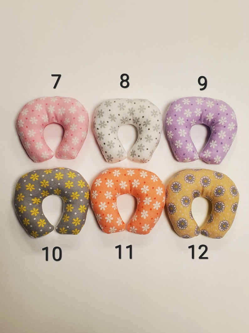 K&ouml;nnte beinhalten: Sechs U-f&ouml;rmige Nackenst&uuml;tzkissen mit verschiedenen Blumenmustern. Die Kissen sind in zwei Reihen mit jeweils drei Kissen angeordnet. Die obere Reihe hat rosa, graue und lila Kissen. Die untere Reihe hat graue, orange und gelbe Kissen. Jedes Kissen hat eine Nummer von 7 bis 12 aufgedruckt.
