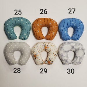 K&ouml;nnte beinhalten: Sechs verschiedene gemusterte Nackenst&uuml;tzkissen in verschiedenen Farben, darunter Grau, Blau, Orange und Wei&szlig;. Die Kissen sind von 25 bis 30 nummeriert.