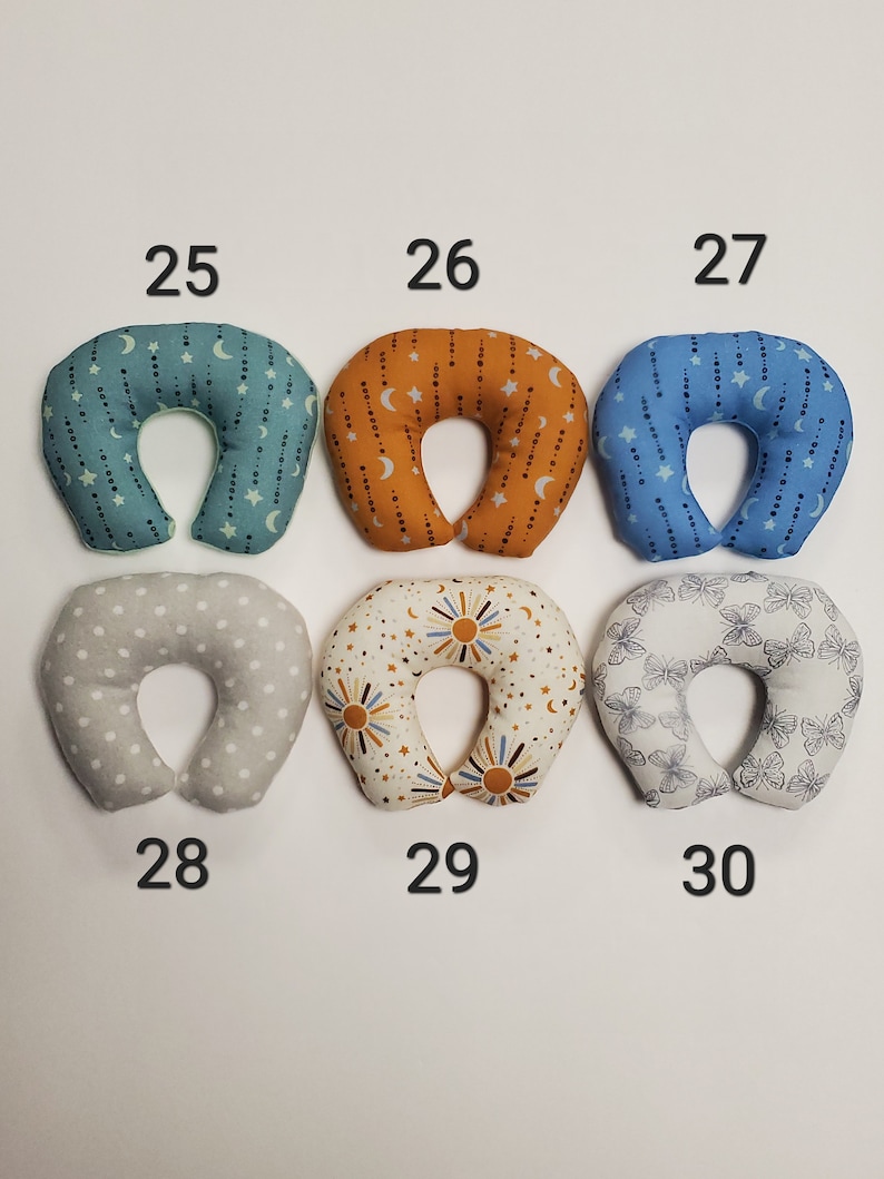 K&ouml;nnte beinhalten: Sechs verschiedene gemusterte Nackenst&uuml;tzkissen in verschiedenen Farben, darunter Grau, Blau, Orange und Wei&szlig;. Die Kissen sind von 25 bis 30 nummeriert.
