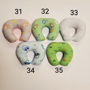 K&ouml;nnte beinhalten: F&uuml;nf verschiedene Nackenst&uuml;tzkissen f&uuml;r Babys mit verschiedenen Mustern. Die Kissen sind hufeisenf&ouml;rmig und aus weichem Stoff gefertigt. Die Muster umfassen Autos, B&auml;ren und Buchstaben.