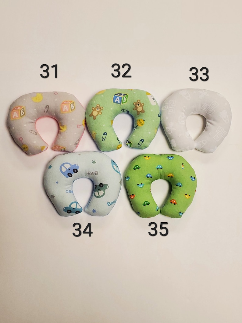 K&ouml;nnte beinhalten: F&uuml;nf verschiedene Nackenst&uuml;tzkissen f&uuml;r Babys mit verschiedenen Mustern. Die Kissen sind hufeisenf&ouml;rmig und aus weichem Stoff gefertigt. Die Muster umfassen Autos, B&auml;ren und Buchstaben.