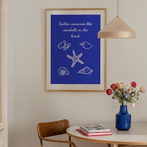 May include: A framed print with a blue background features white line drawings of seashells and a starfish. The text "Gather memories like seashells on the beach" is above the illustrations. A vase of flowers sits on a round table.