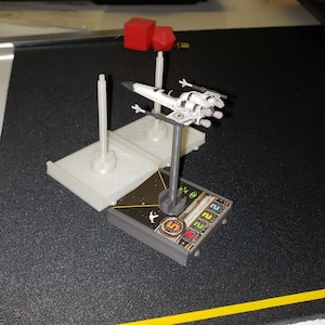 Op de afbeelding: Een witte en zwarte X-Wing-sterrenjager miniatuur met een grijze basis en een zwart-witte geprinte basis met de tekst "K-Wing 1.0 RELIC" en de nummers 2, 2, 2, 5.