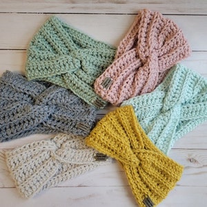 May include: Five crocheted headbands in different colors: gray, light green, pink, light blue, and yellow. Each headband has a twisted knot design.