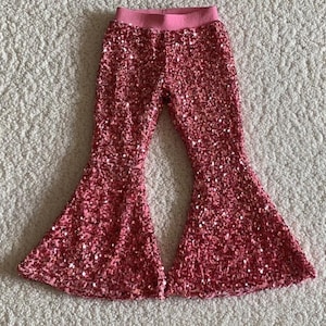 May include: Pink sequined bell bottom pants for a child. The pants have a wide leg opening and are made of a soft, sparkly fabric.