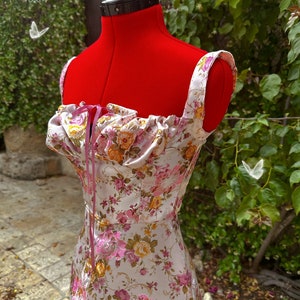 May include: A white satin dress with a floral print and pink straps. The dress has a gathered neckline and a fitted bodice.