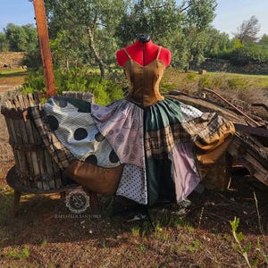 Könnte beinhalten: Ein braunes Patchworkkleid mit verschiedenen Mustern, darunter Punkte, Karos und Wirbel. Das Kleid wird auf einer Schaufensterpuppe in einer rustikalen Umgebung im Freien präsentiert.