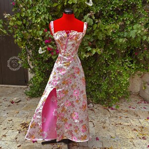 May include: A pink and white floral print dress with a pink satin lining and a front slit. The dress has a sweetheart neckline and thin straps.