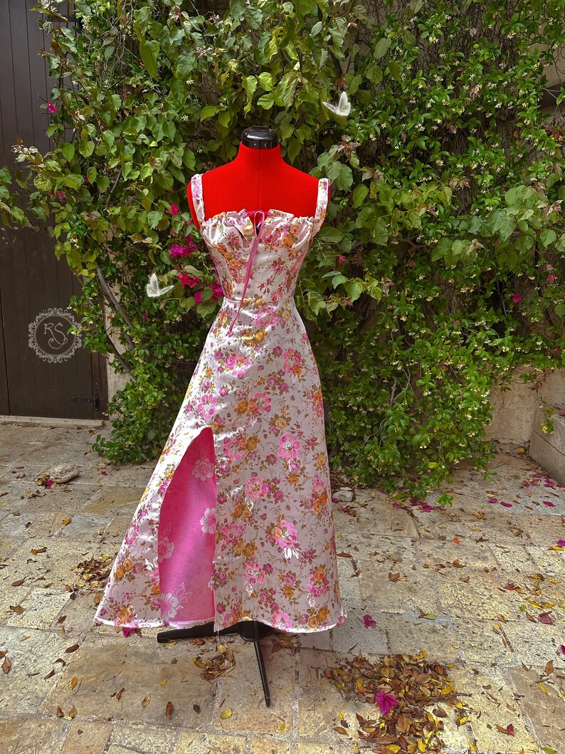 May include: A pink and white floral print dress with a pink satin lining and a front slit. The dress has a sweetheart neckline and thin straps.
