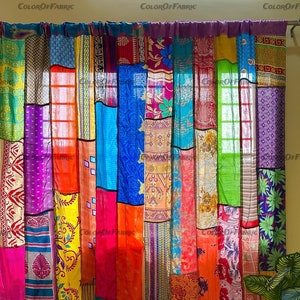 Può includere: Una tenda colorata a patchwork realizzata con tessuto riutilizzato. La tenda è composta da molti colori e motivi diversi, tra cui rosso, arancione, giallo, verde, blu, viola e rosa. La tenda è appesa a una parete bianca e ha un tappeto marrone davanti.