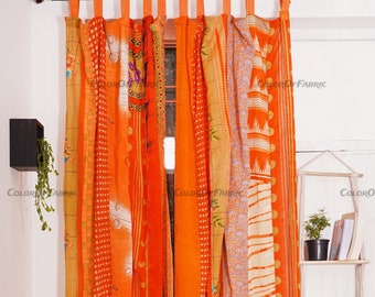 May include: A set of orange-toned curtains featuring a patchwork of vertical fabric strips with various patterns including dots, floral motifs, and stripes. The curtains are hung from a metal rod using fabric tabs at the top edge.