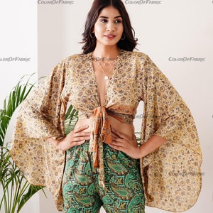 May include: A woman wearing a beige and brown floral print top with a tie front and bell sleeves. She is also wearing green paisley print shorts.
