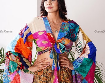 May include: A colorful patchwork top with long sleeves and a tie front. The top is made of different fabrics in various colors, including pink, blue, green, orange, and red. The top is tied at the waist and has a relaxed fit.
