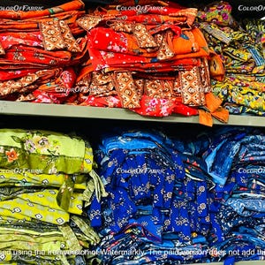 May include: A shelf with stacks of colorful fabric. The fabric is in various patterns and colors, including red, orange, yellow, green, blue, and white. The fabric is folded and stacked neatly on the shelf. The shelf is made of metal and has a light gray finish.