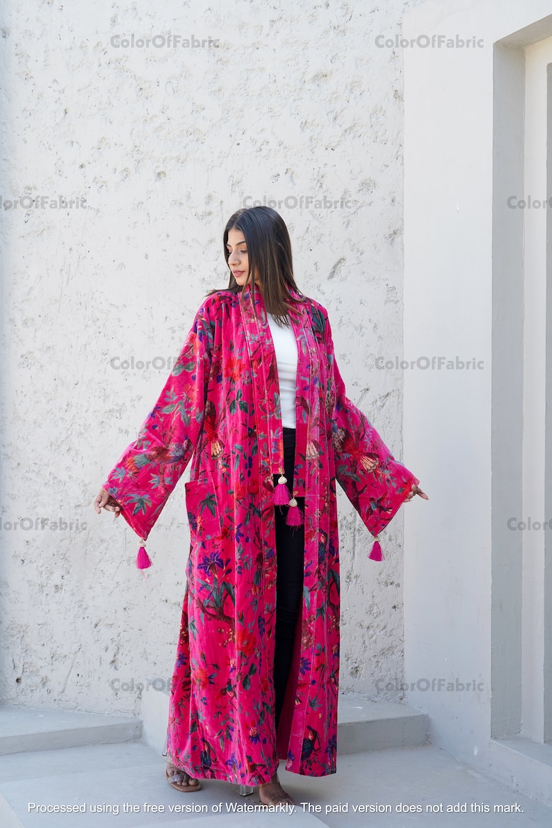 May include: A long, pink velvet robe with a floral print and tassels. The robe has a shawl collar and a tie belt.