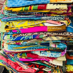 May include: A stack of colorful fabric scraps with various patterns and textures. The fabric is folded neatly and arranged in a vertical stack. The fabric is a mix of bright colors, including yellow, blue, pink, green, and red.