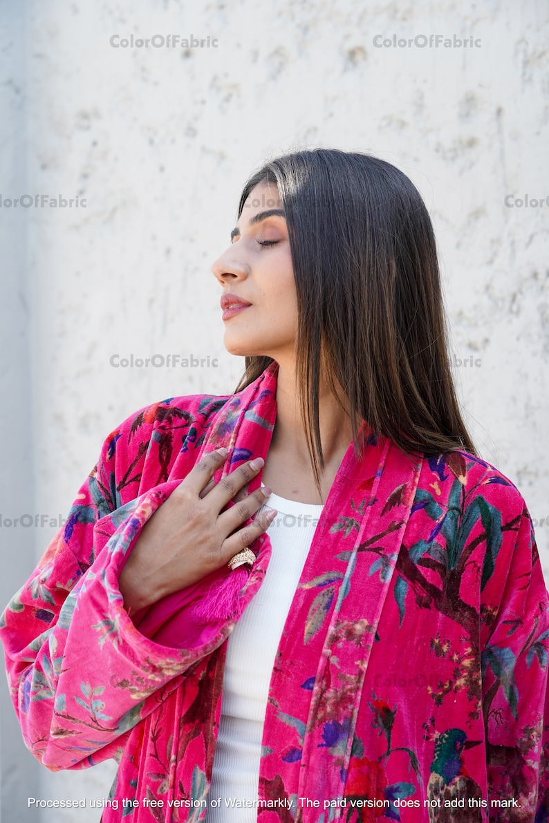May include: A pink velvet kimono with a floral print featuring birds and leaves. The kimono has a tassel on the left side and is open in the front.