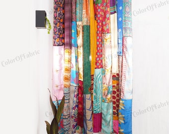 May include: A colorful patchwork curtain made from repurposed saris. The curtain is made up of various fabrics in shades of pink, blue, green, yellow, and red. The curtain is hung on a white wall.