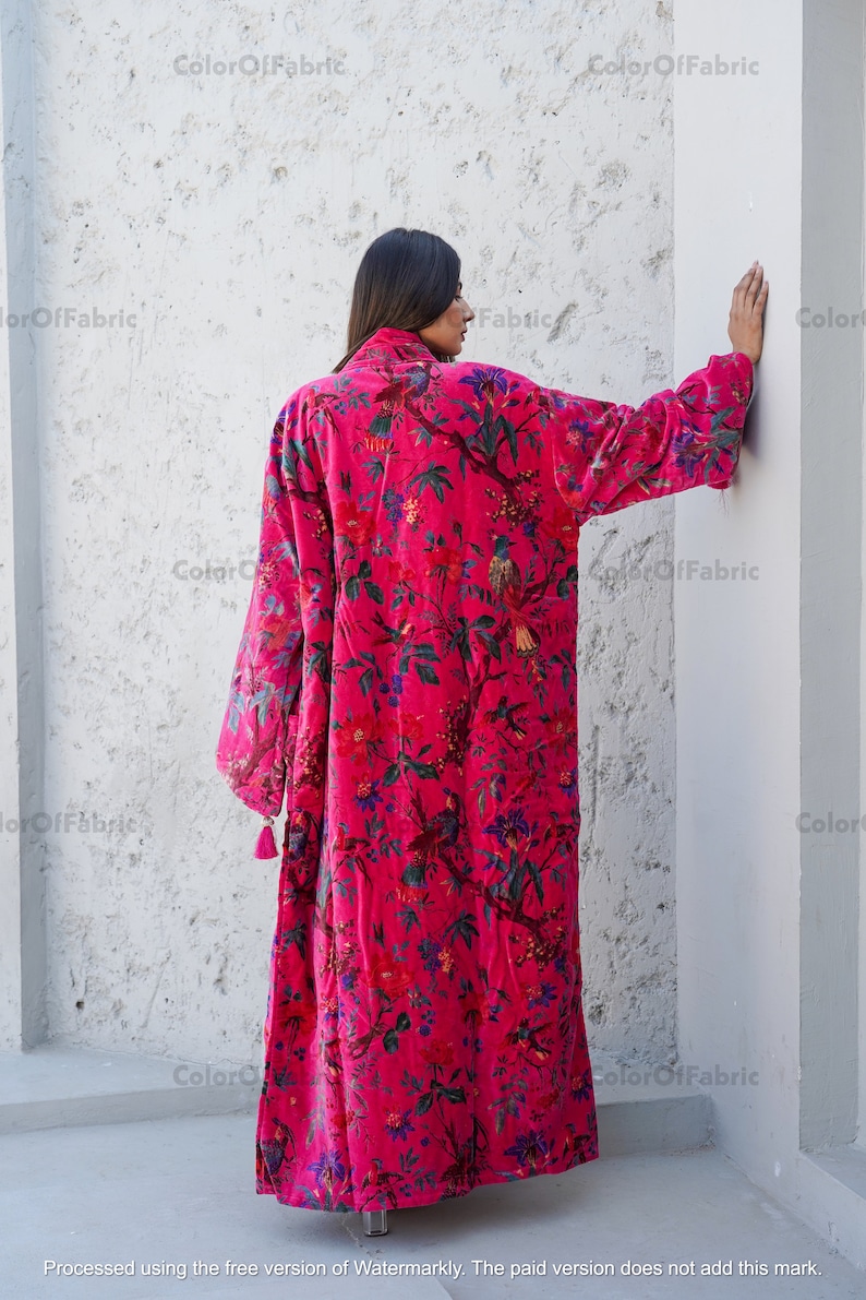 May include: A long, pink velvet robe with a floral and bird print. The robe has long sleeves and a tassel detail at the cuffs.