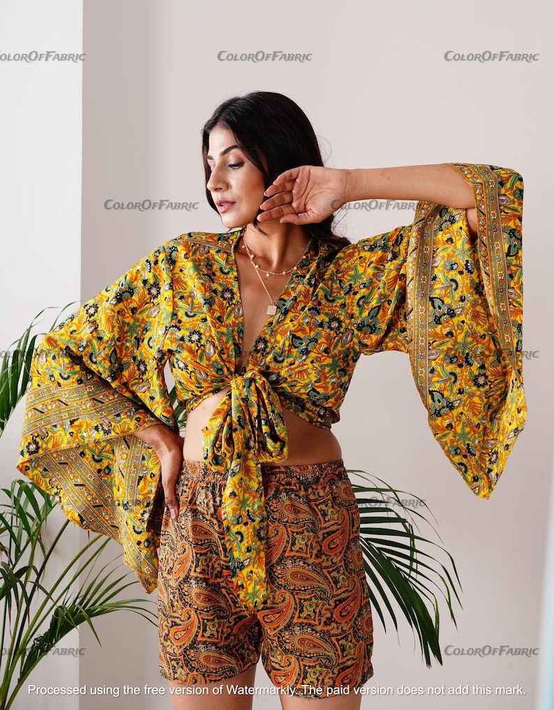 May include: A yellow and green floral print crop top with a tie front and wide bell sleeves. The top is paired with matching yellow and green floral print shorts with a paisley pattern.