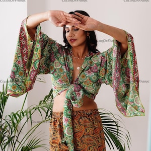 May include: A green and orange paisley print top with long sleeves and a tie front. The top is made of a lightweight fabric and has a relaxed fit.