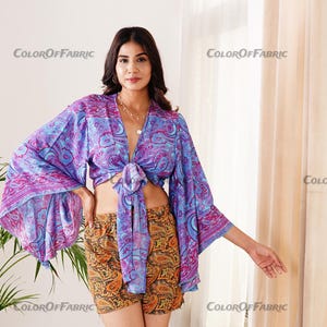 May include: A purple and blue patterned crop top with long sleeves and a tie at the front. The top is worn with a matching patterned skirt.