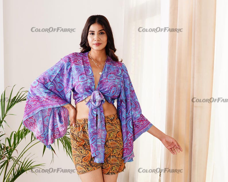 May include: A purple and blue patterned crop top with long sleeves and a tie at the front. The top is worn with a matching patterned skirt.