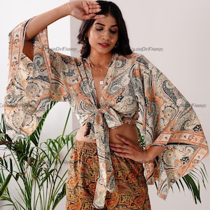 May include: A paisley print crop top with a tie front and long, wide sleeves. The top is made of a lightweight fabric and has a relaxed fit. The model is wearing the top with a matching paisley print skirt.