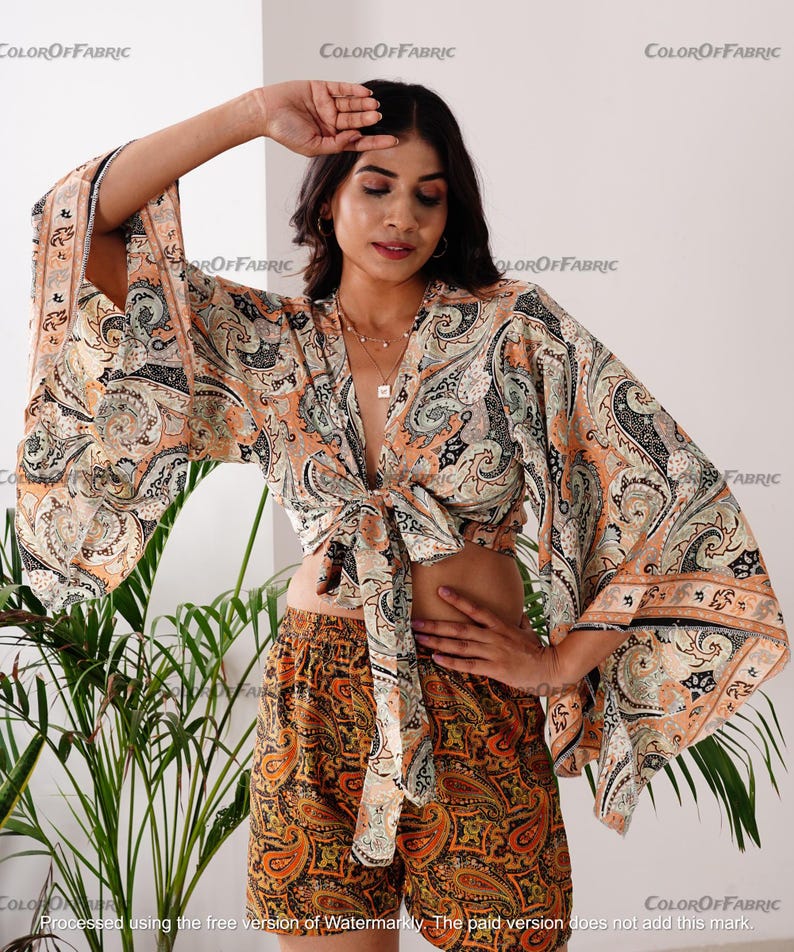 May include: A paisley print crop top with a tie front and long, wide sleeves. The top is made of a lightweight fabric and has a relaxed fit. The model is wearing the top with a matching paisley print skirt.