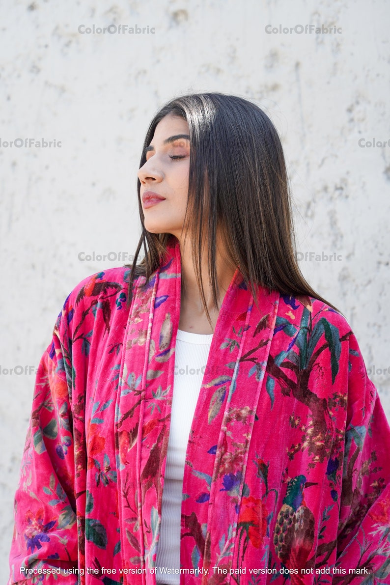 May include: A woman wearing a pink velvet kimono with a floral and bird print. The kimono has a white lining and is open in the front.