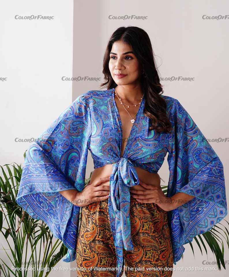May include: A blue and turquoise paisley print crop top with long bell sleeves. The top is tied at the front and has a deep V-neckline.
