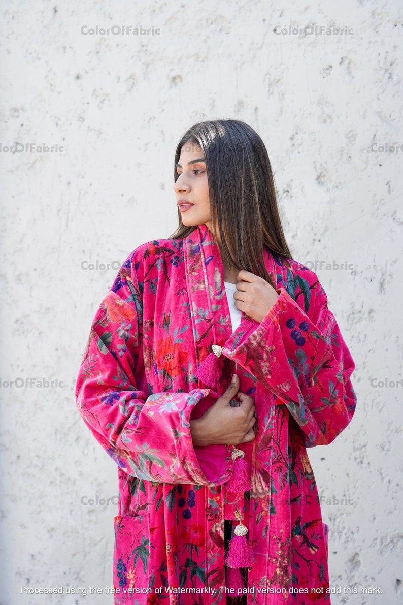 May include: A pink velvet robe with a floral print and tassel accents. The robe has long sleeves and a shawl collar.
