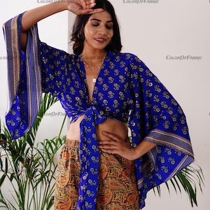 May include: A blue and gold patterned crop top with a tie front and wide sleeves. The top is paired with orange and brown paisley print shorts.