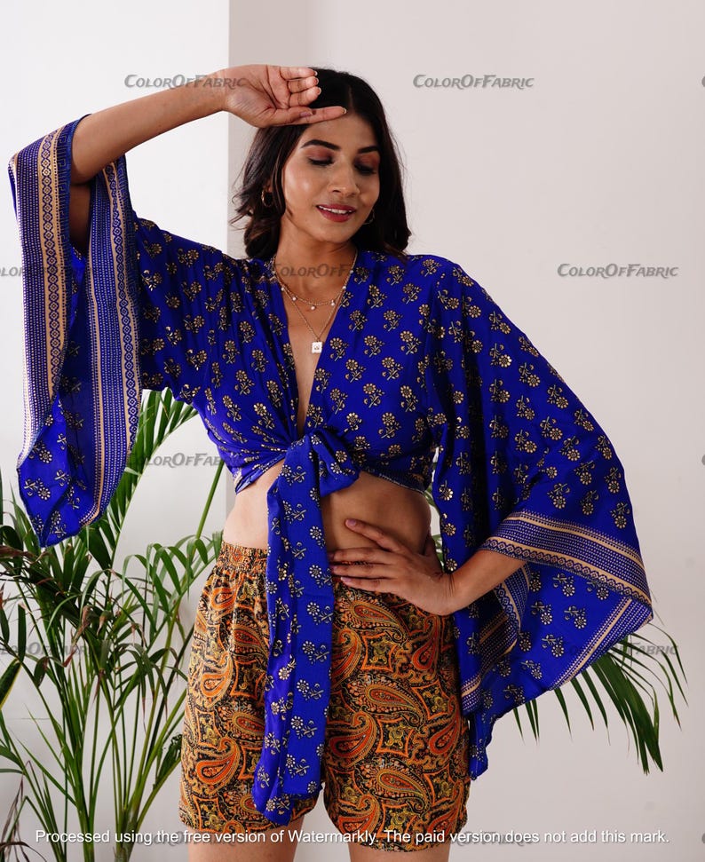 May include: A blue and gold patterned crop top with a tie front and wide sleeves. The top is paired with orange and brown paisley print shorts.