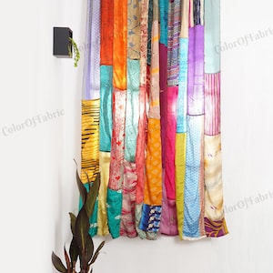 Puede incluir: Una cortina de patchwork colorida hecha de varias telas en tonos de azul, verde, naranja, rosa, morado y amarillo. La cortina está colgada en una pared blanca con una pequeña planta en maceta en la esquina.