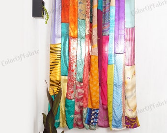 May include: A colorful patchwork curtain made of various fabrics in shades of blue, green, orange, pink, purple, and yellow. The curtain is hung on a white wall with a small potted plant in the corner.