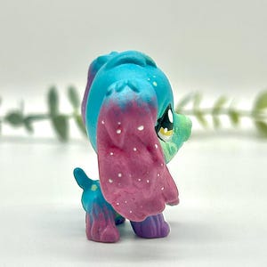 Peut inclure: Figurine de chien jouet color&eacute;e avec une t&ecirc;te et des oreilles bleues, passant au rose avec des mouchetures blanches. Le corps est un m&eacute;lange de bleu, de vert et de violet. C'est un objet de collection.