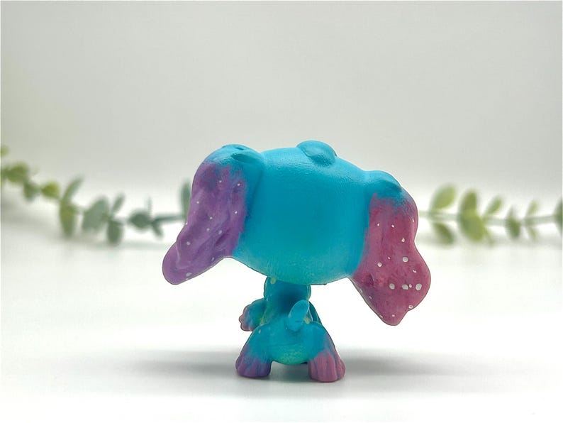 Peut inclure: Petite figurine turquoise repr&eacute;sentant un animal aux grandes oreilles. Les oreilles sont peintes en violet avec des mouchetures blanches et les pointes sont roses. La figurine a une petite queue.