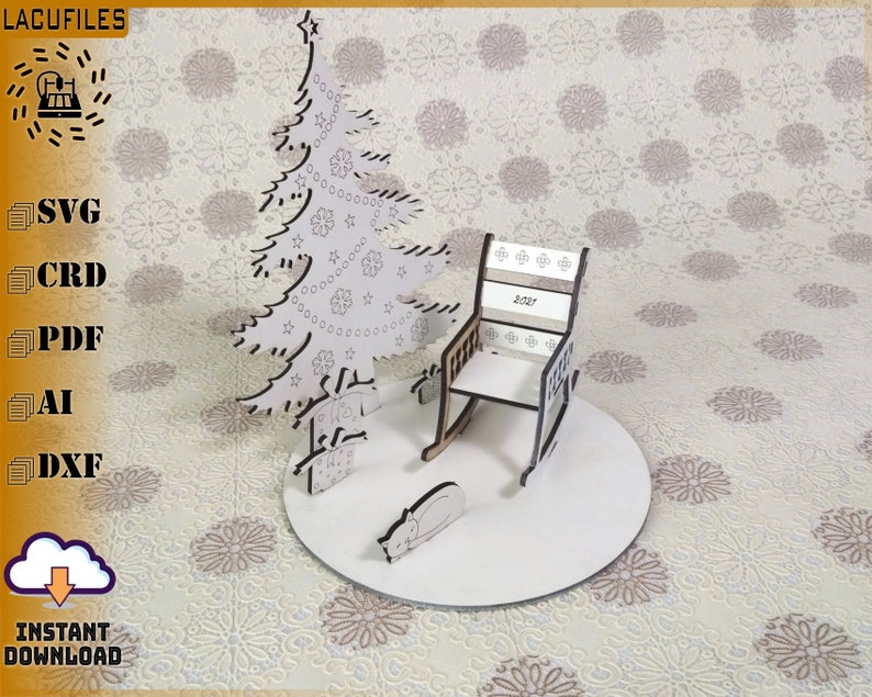 May include: A laser-cut wooden Christmas scene featuring a tree, rocking chair, and sleeping cat on a circular base. The chair back displays "2021". The tree is decorated with stars and ornaments. The scene is set on a patterned background.