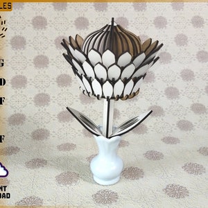 May include: A white and brown wooden flower with layered petals in a white ceramic vase. The flower is made of multiple pieces of wood that are layered together to create a 3D effect. The vase is simple and elegant, with a rounded base and a narrow neck.