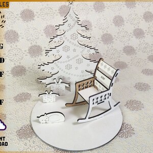 May include: A laser-cut Christmas scene featuring a tree, presents, a rocking chair, and a sleeping cat. The rocking chair has the year 2021 on the back. The scene is on a white circular base. The image also includes the text "LACUFILES" and "INSTANT DOWNLOAD".