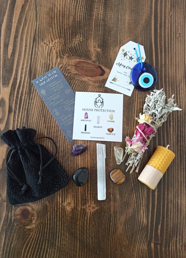 May include: A house protection kit containing crystals, a sage smudge stick, a candle, and a small black pouch. The crystals include amethyst, selenite, citrine, obsidian, and tiger's eye. The kit also includes a card with the text "House Protection" and a list of the crystals. The card also includes the text "EyeDesignbyLC".