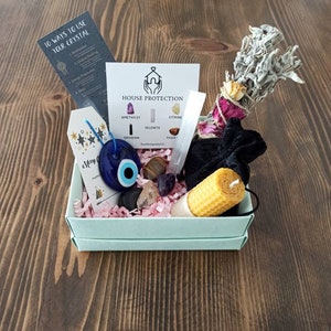 May include: A light blue box filled with crystals, a sage bundle, a yellow candle, and a blue evil eye charm. The box is labelled "House Protection" and lists the crystals included: amethyst, citrine, selenite, obsidian, and tiger's eye.