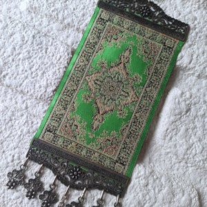 May include: A green and gold patterned fabric wall hanging with a metal frame and tassels. The hanging features a blue glass ornament.