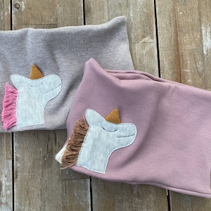 May include: Two ribbed knit neck warmers, one gray and one mauve, each adorned with a unicorn applique. The unicorns have a gray face, a gold horn, and a pink or brown mane. The gray warmer has a small label that says "Petit Nie".