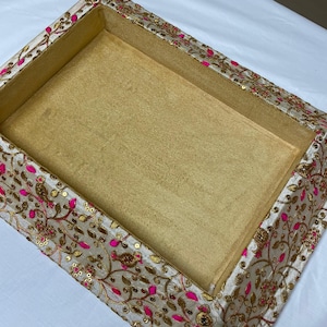 May include: A white and gold decorative box with pink floral embroidery and sequins. The box is empty and has a gold velvet lining.