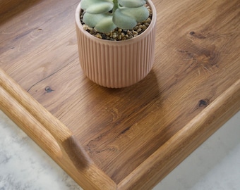 May include: A rectangular wooden serving tray with a natural grain finish and integrated handles, featuring a small, pale pink, vertically ribbed ceramic pot containing a light green succulent plant with rounded leaves and small pebbles.