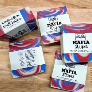 May include: Several bars of handcrafted soap with red, white, and blue swirls. Each bar is wrapped with a white label that reads "MAFIA Stripes" and "HANDCRAFTED SOAP BAR". One bar has the text "handmade in small batches BUFFALO, NY".
