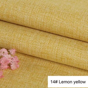 May include: A folded piece of lemon yellow fabric with a visible woven texture. The material features a consistent, coarse weave pattern throughout. A small cluster of light pink flowers is visible in the lower left corner. Text reads 14# Lemon yellow.