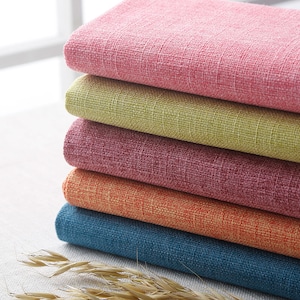 May include: A stack of five fabric swatches in different colors: pink, green, burgundy, orange, and blue. The fabric has a textured, woven look.